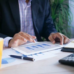 Person working on financial reports at desk with tablet and notepad